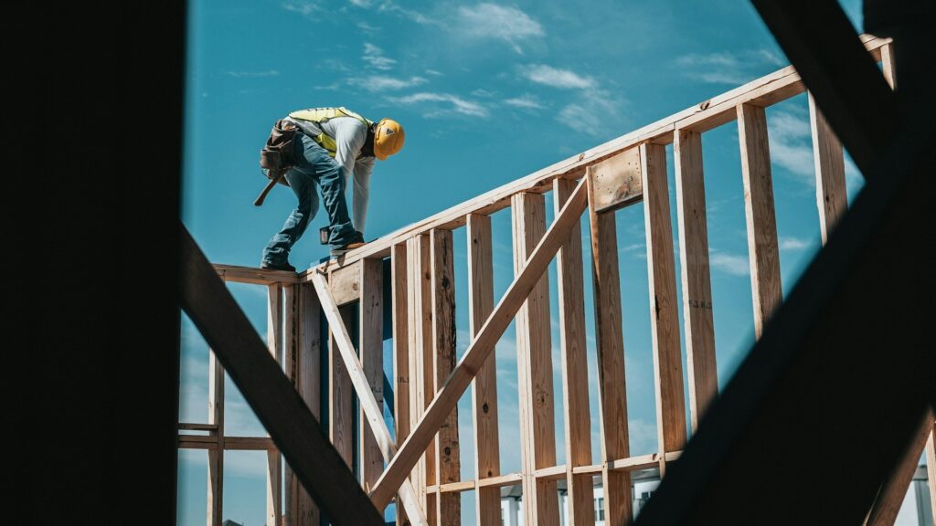 Bouwvakker werkt aan houten constructie van een aanbouw onder een heldere blauwe lucht