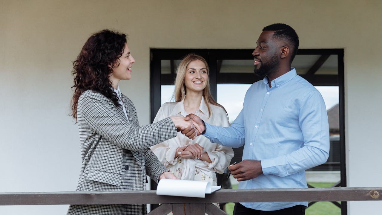 Drie mensen bij een woning, twee schudden handen na succesvolle bezichtigingen